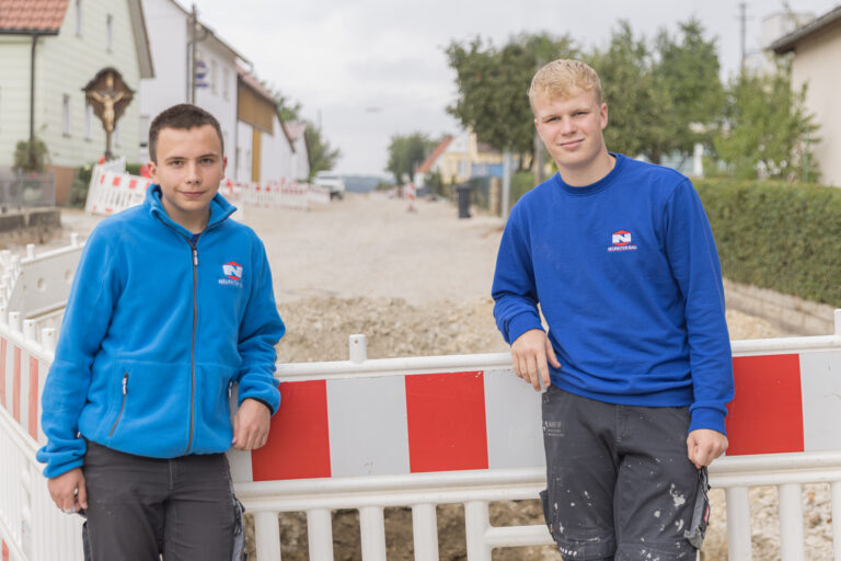 Zwei Auszubildende im Straßenbau bei Neureiter-Bau in Fremdingen, vor einer Baustelle mit Absperrung