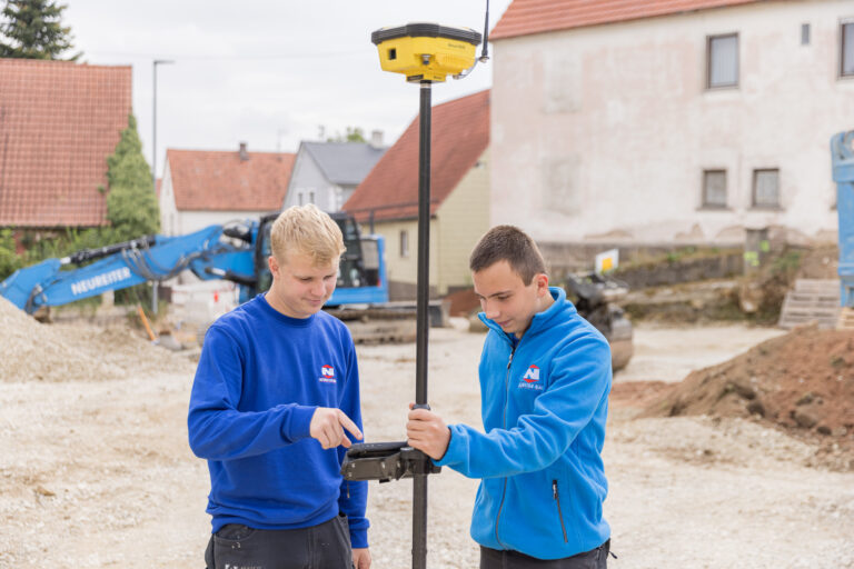 Zwei Auszubildende bei Neureiter-Bau nehmen auf der Baustelle ein Aufmaß mit moderner Messtechnik.