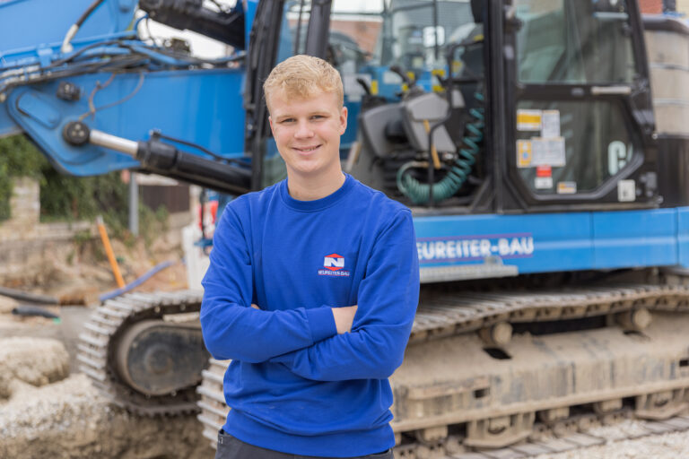 Azubi Mathias im dritten Ausbildungsjahr zum Maurer bei Neureiter Bau – vor einer Baumaschine auf der Baustelle.